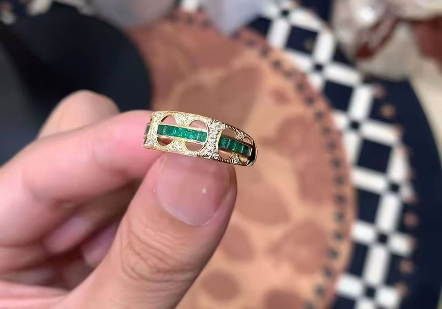 Open band ring with green stones, held in hand