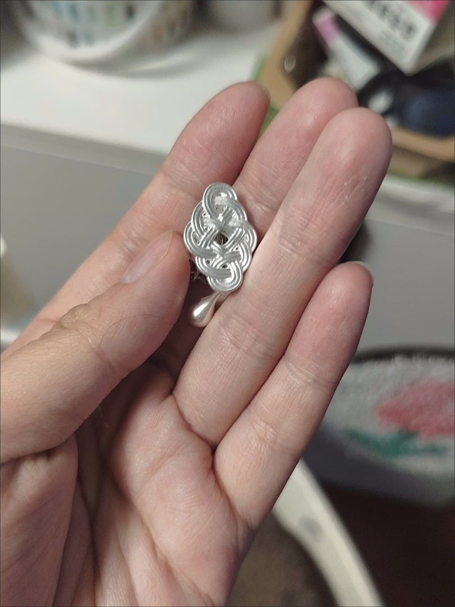 Silver-tone knot drop earring held in the palm