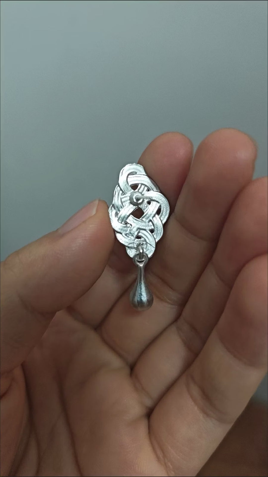 Silver-tone knot drop earring held in the palm
