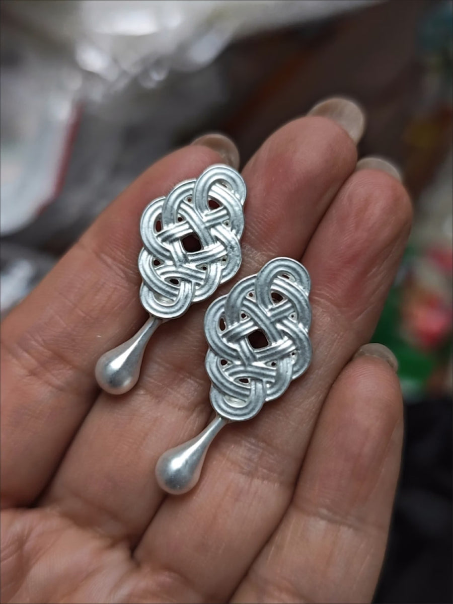 Pair of silver-tone knot drop earrings held in the palm
