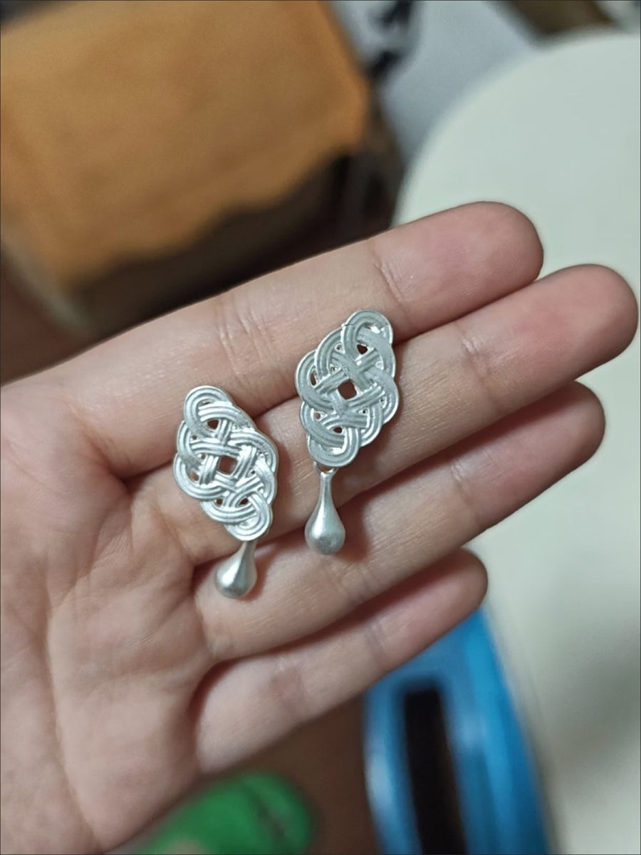 Pair of silver-tone knot drop earrings held in the palm