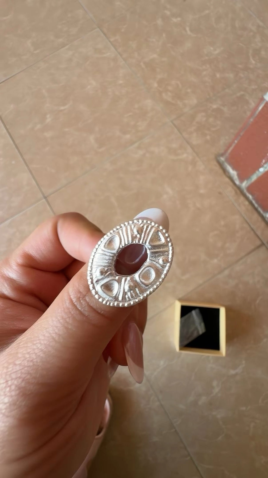 Oval textured silver-tone ring held in hand